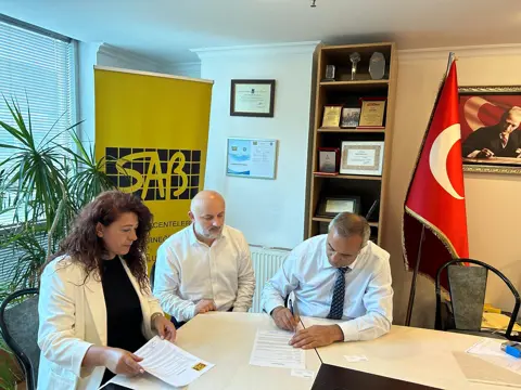 SAB ofisinde üç kişi, gayrimenkul değerleme protokolünü imzalarken
