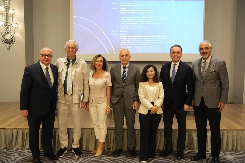 Etkinlik katılımcıları, sunum ekranı önünde ayakta grup fotoğrafında