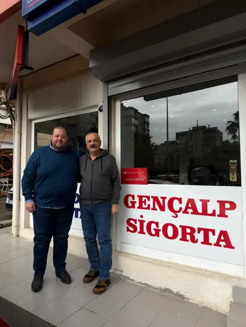 Gençalp Sigorta tabelası önünde iki kişi yan yana duruyor
