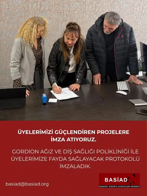 BASİAD protokol imza töreninde bir kadın belge imzalıyor, iki kişi izliyor